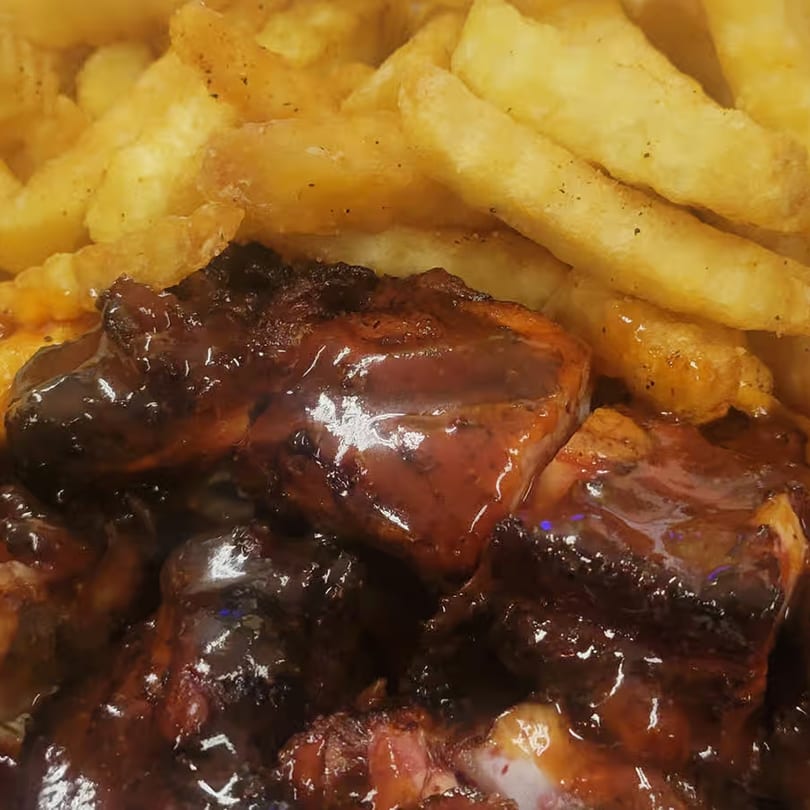 Close-up of ChicknCoop's fried chicken pieces coated in dark sauce, served with golden french fries.