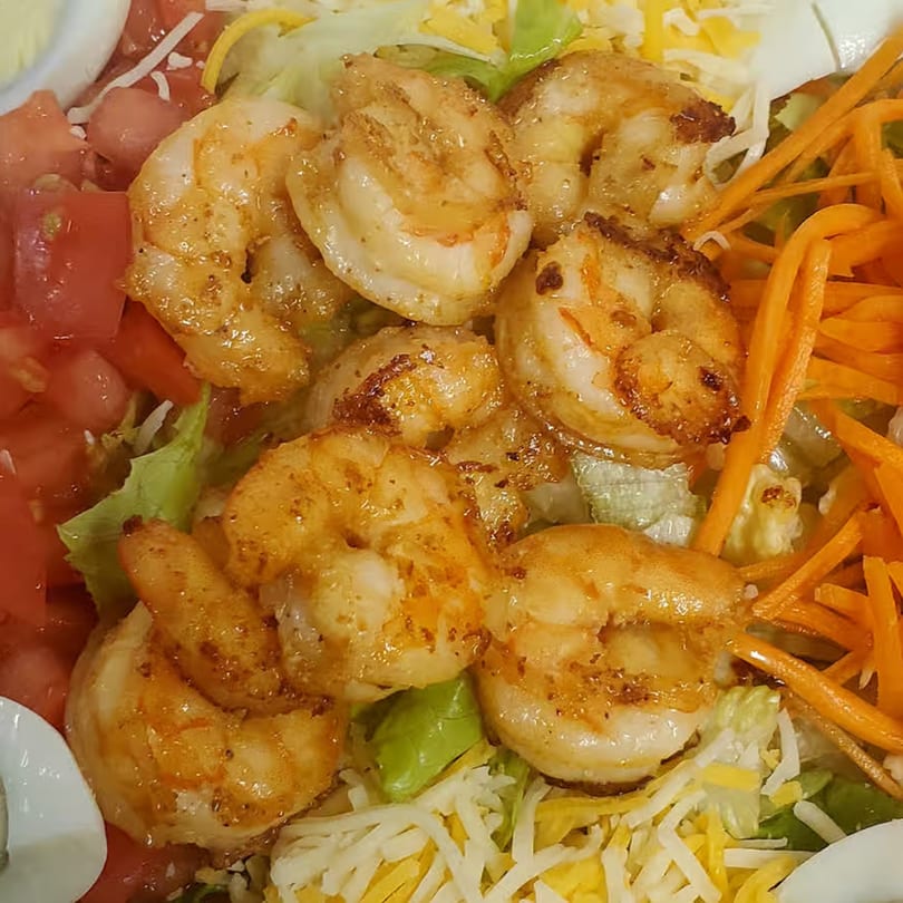 Close-up of a fresh salad with grilled shrimp, diced tomatoes, shredded carrots, and cheese.