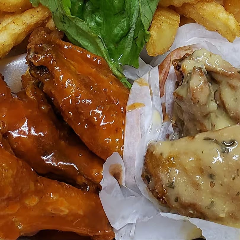 Two flavors of ChicknCoop chicken wings, one orange and one creamy, with fries and lettuce.